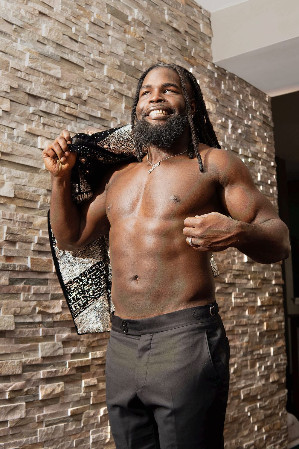 Against a stone wall, pulling a patterned jacket across his shoulders, abs lit, fists up.