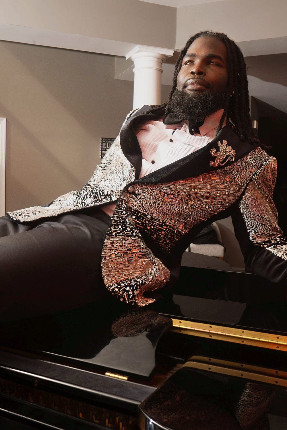 In a bronze sequin tuxedo, reclining across a grand piano between tall columns.