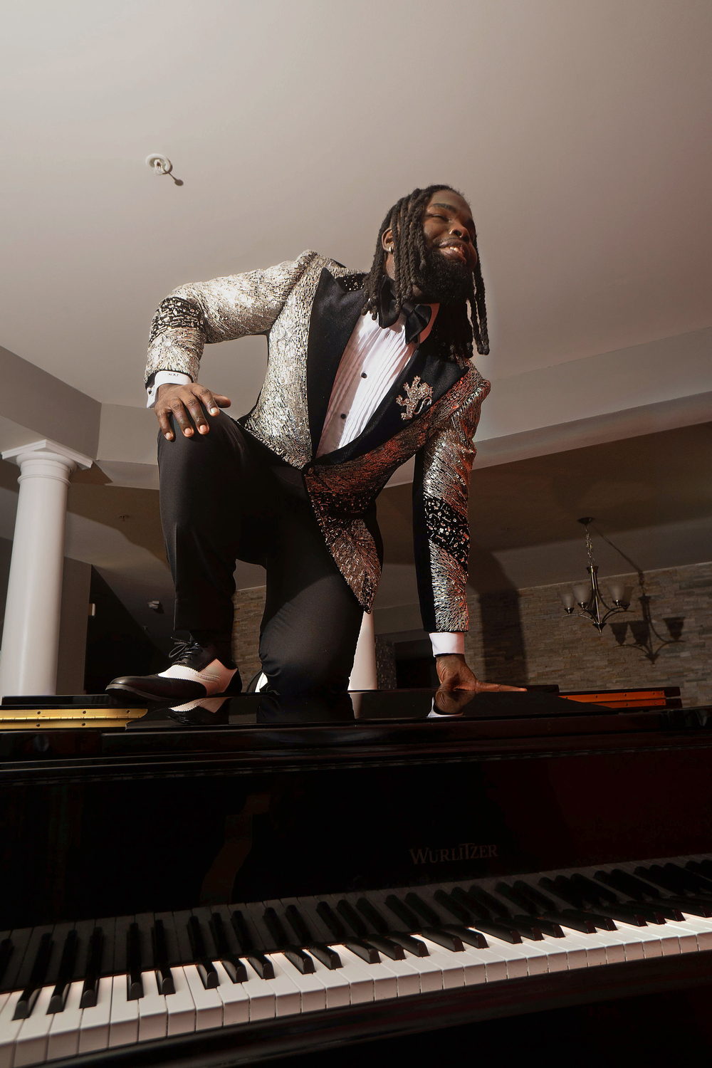 In a sequin tuxedo, crouched low on the lid of a grand piano, framed from the keys up.