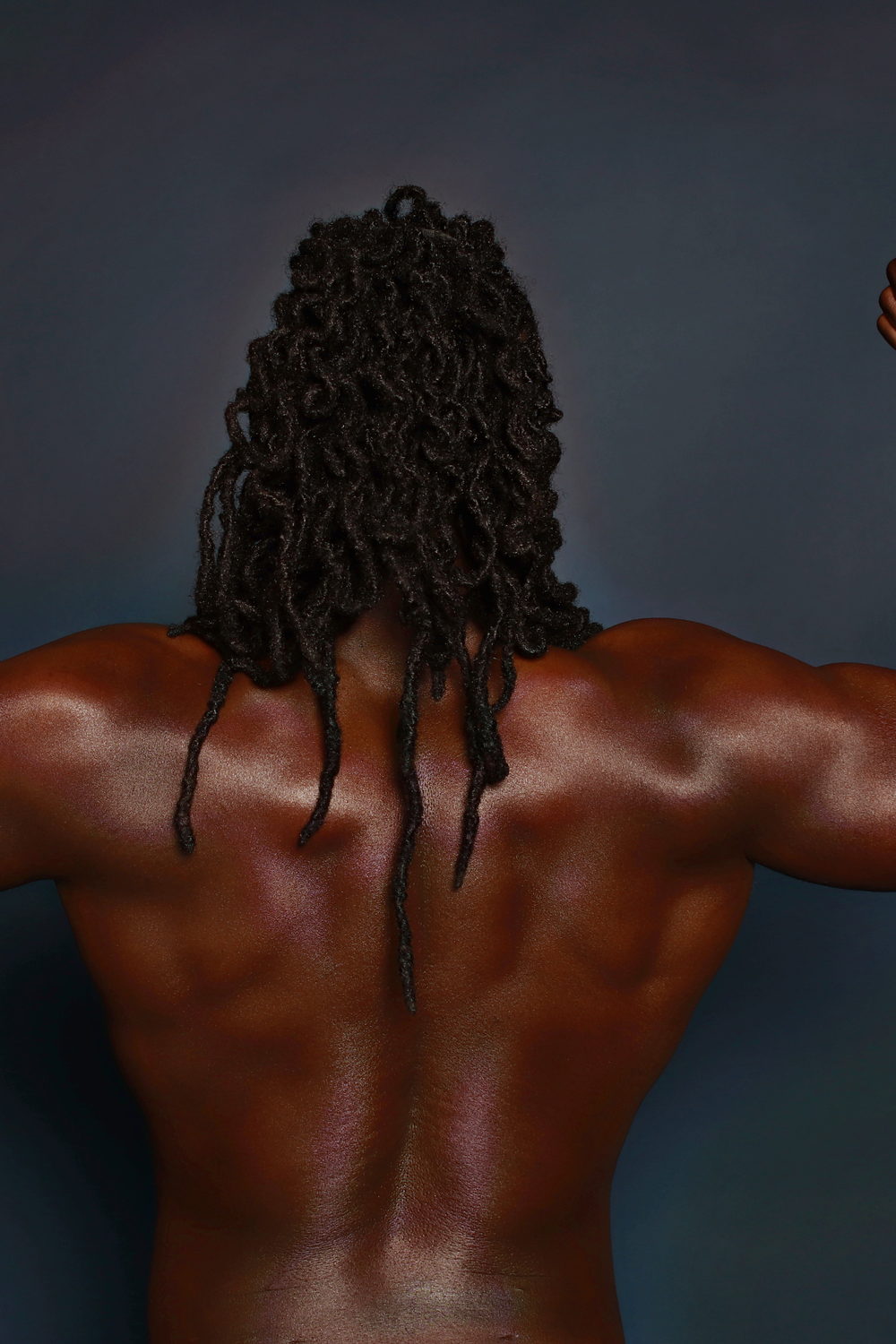 Back to camera in a dark studio, long locs falling down a sculpted back.