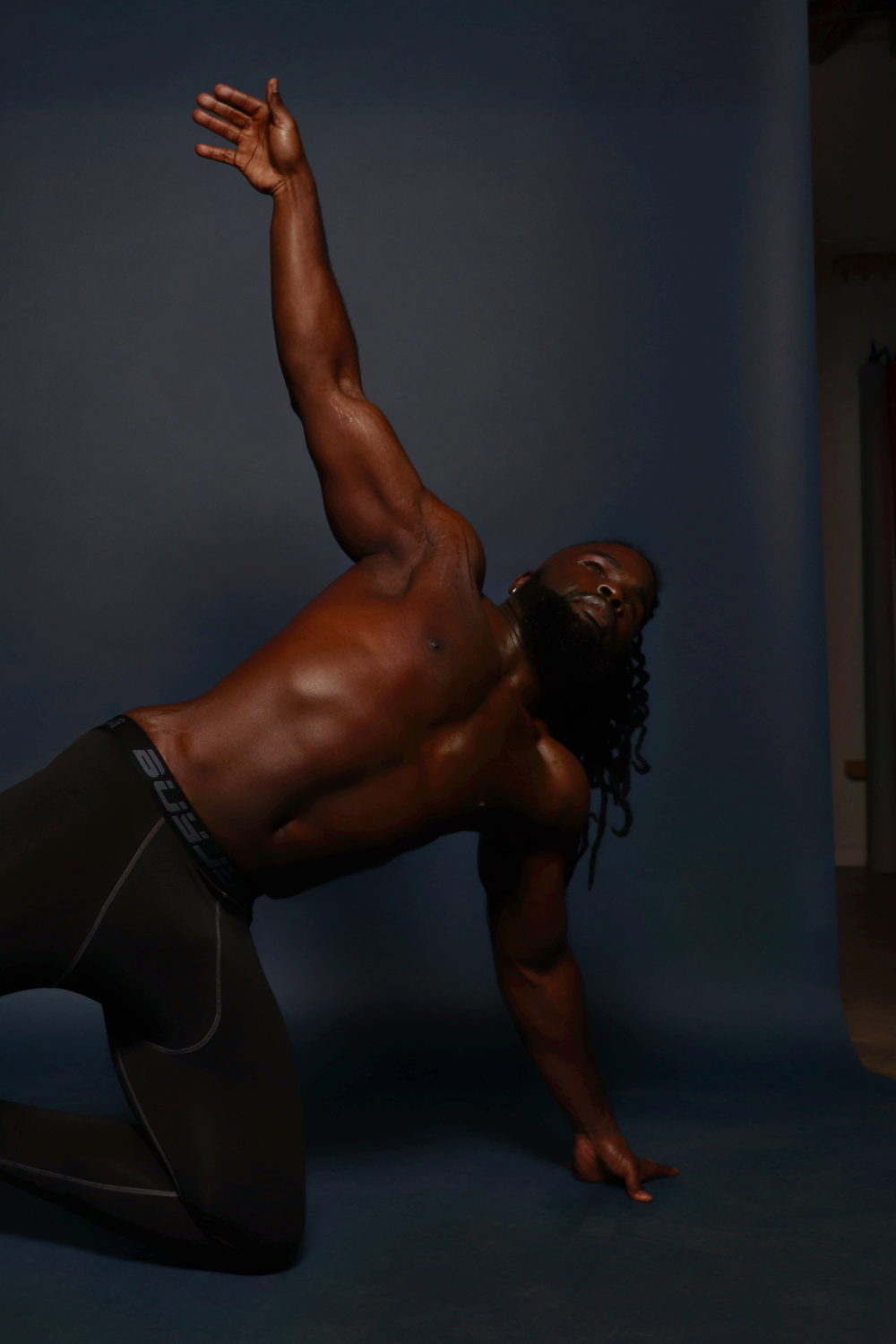 Mid-motion on a blue-lit floor, one arm sweeping overhead in a kneeling reach.