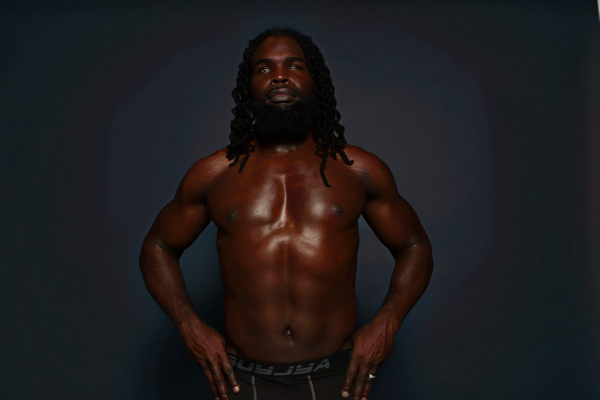 Studio dark, close-up frontal, hands at waist.