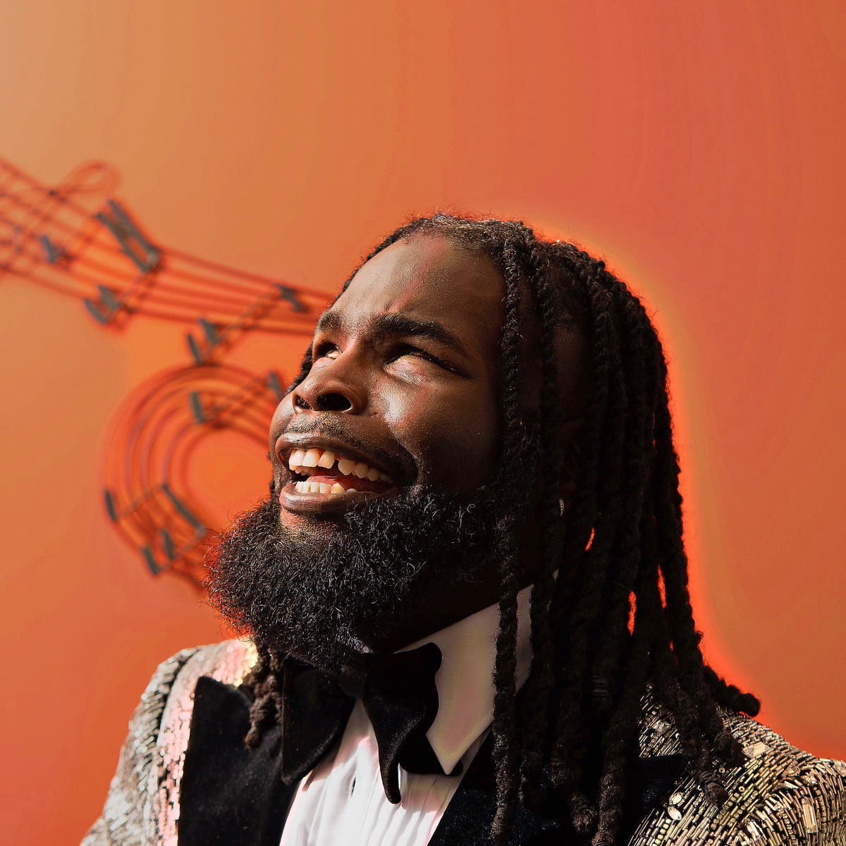In a sequin tuxedo and bow tie, head tipped back mid-song against a warm backdrop.